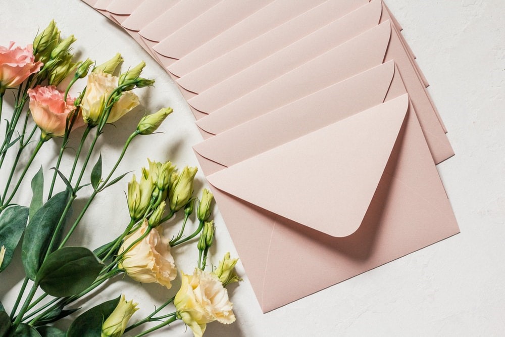 12 beige envelopes on a white surface next to flowers