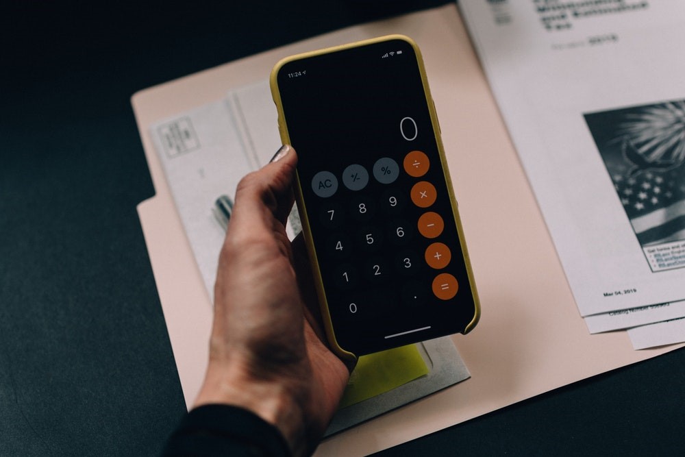 hand holding a black android in yellow case showing calculator app over an open file folder on top of a black desk