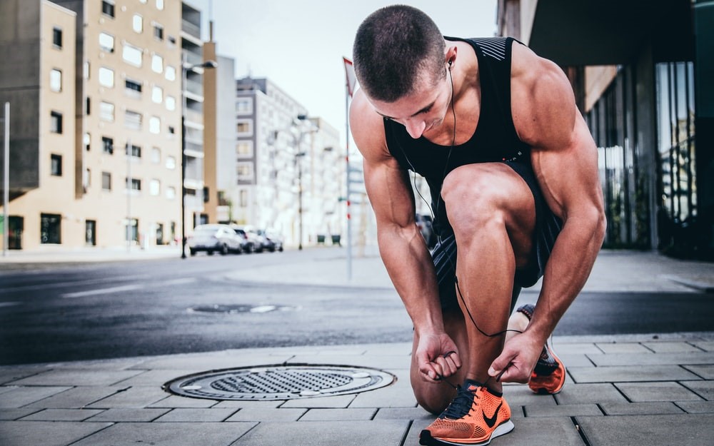 muscular man kneeling to tie shoes of orange Nikes on an urban street