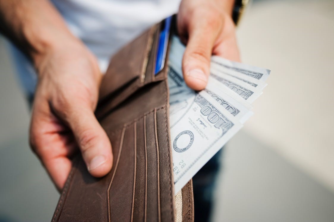 Man holding brown leather wallet with several $100 American bills