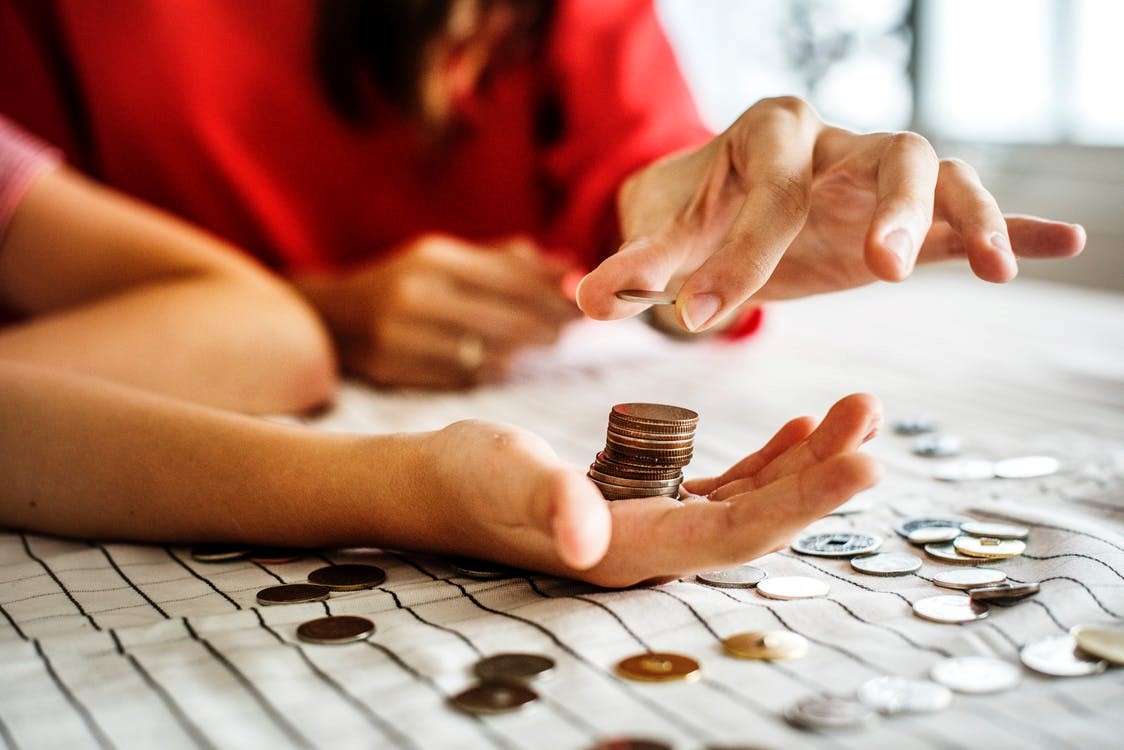 Woman stacking pennies in a child’s hand over a lined tablecloth covered in coins