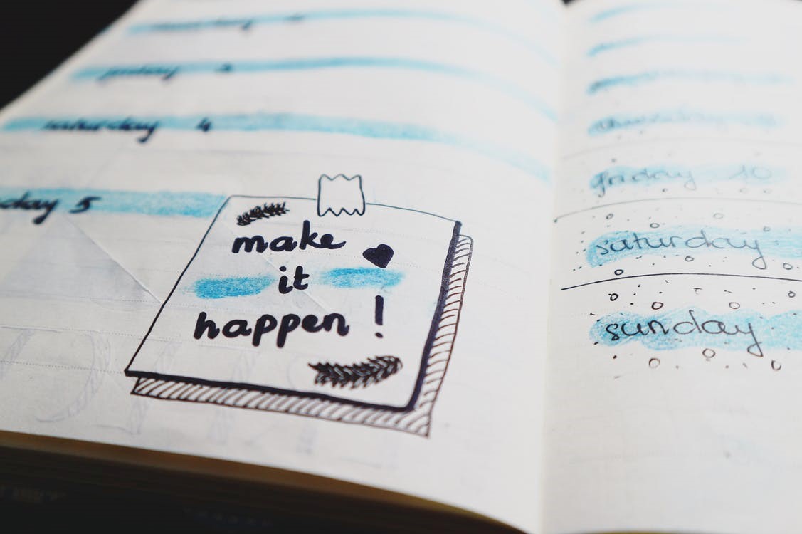 close up on bottom of open notebook page with drawing of a post-it note saying make it happen on it
