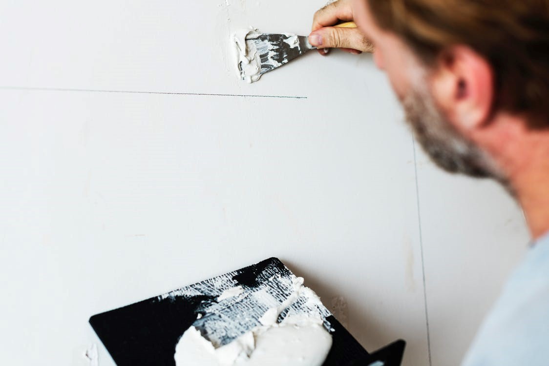 man with beard applying putty with a spatula on drywall