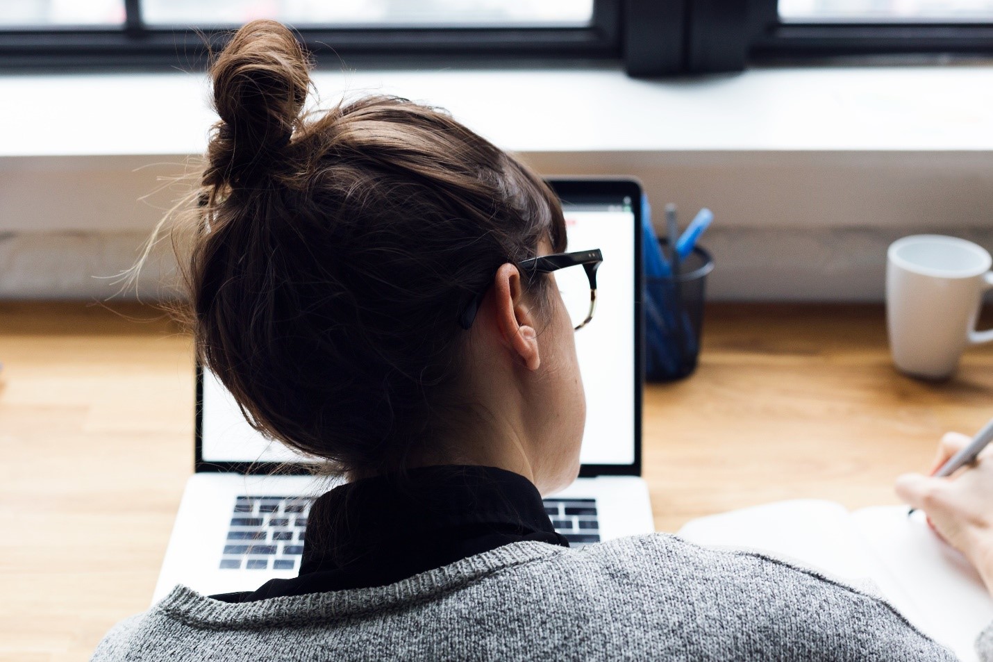 woman with hair in a bun working in front of a laptop on a wooden table
