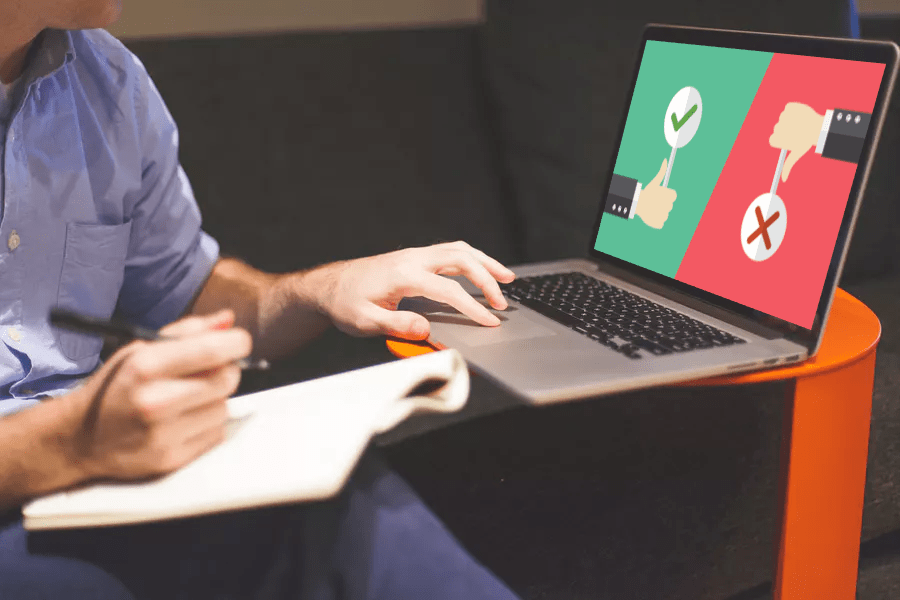 man touching trackpad of a MacBook with left hand and holding a pen on top of notebook in right hand