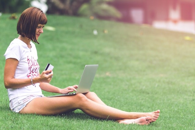 person sitting on grass with credit card in hand and laptop on their lap