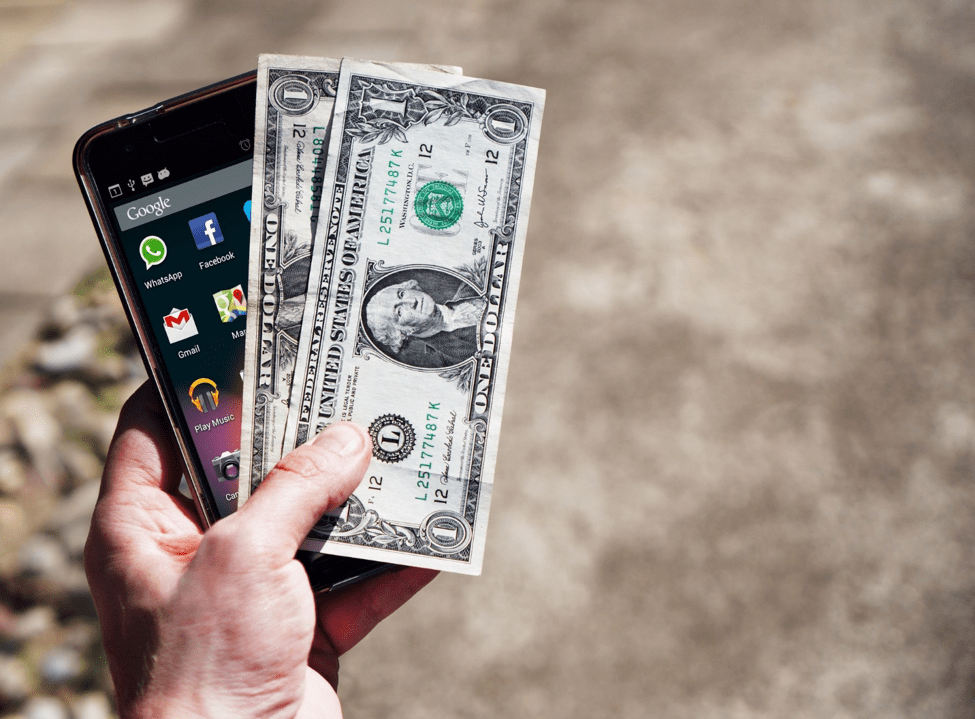 person holding two American dollar bills on top of a smartphone outside